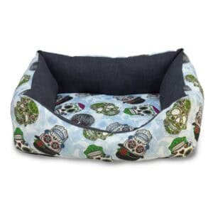 Alto texto: Cama para mascotas con diseño de calaveras coloridas y detalles de tela suave.