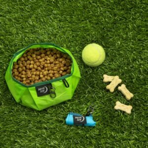 Bolsa de comida para perros con croquetas, pelota de tenis y huesos de juguete en césped artificial.